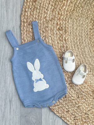 Petrol blue bunny romper with white bow pram shoes on a brown wicker rug.