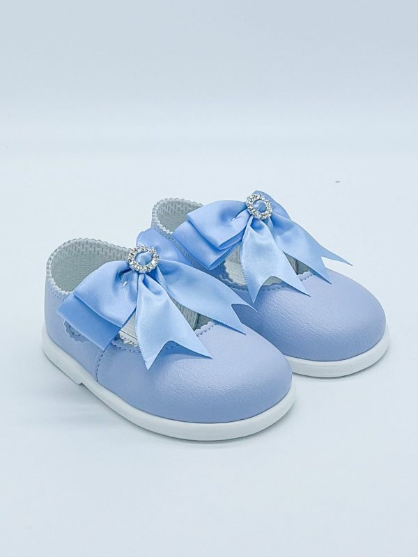Blue patent leather shoes with a large satin bow to the strap & diamanté ring to the centre on a white background facing to the right.