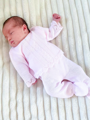 Sleeping baby on a white fluffy blanket; wearing a pink scallop knitted two piece.